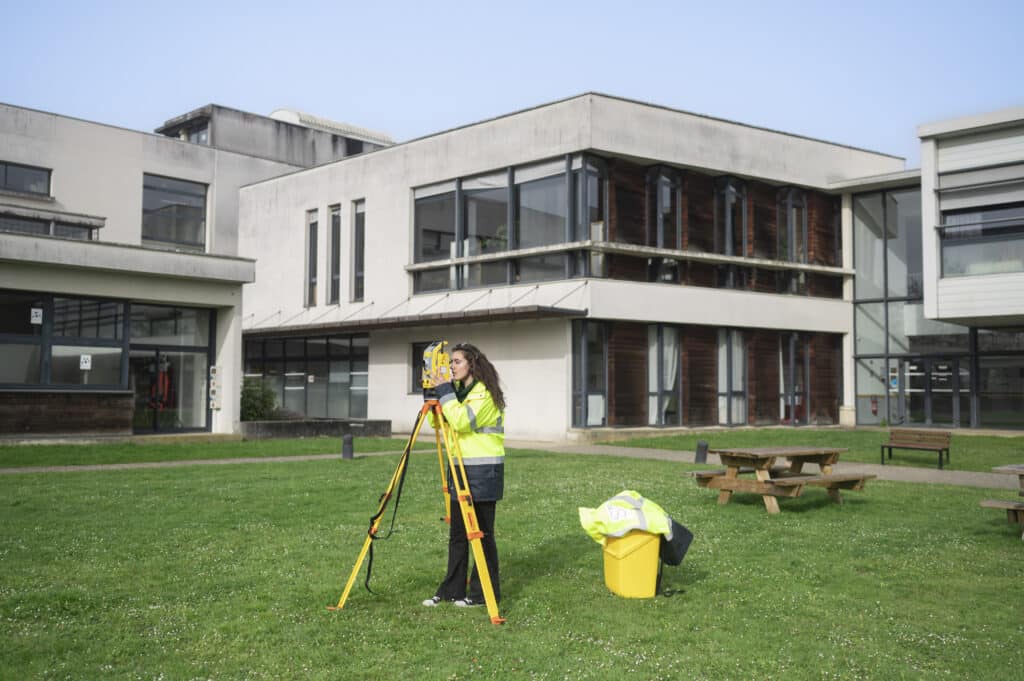 Élève en gilet de sécurité réalise un relevé topographique devant le campus du Mans