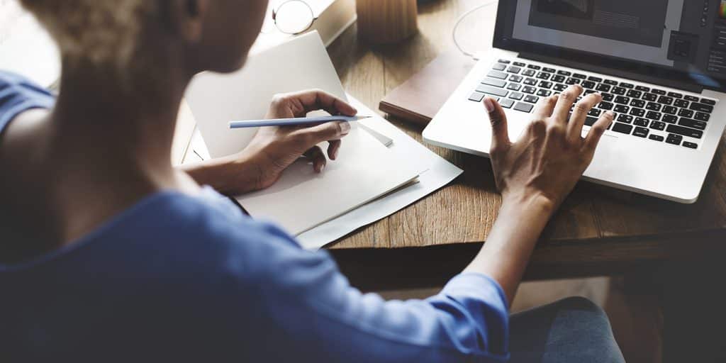 Personne qui prend des notes à côté d'un ordinateur portable