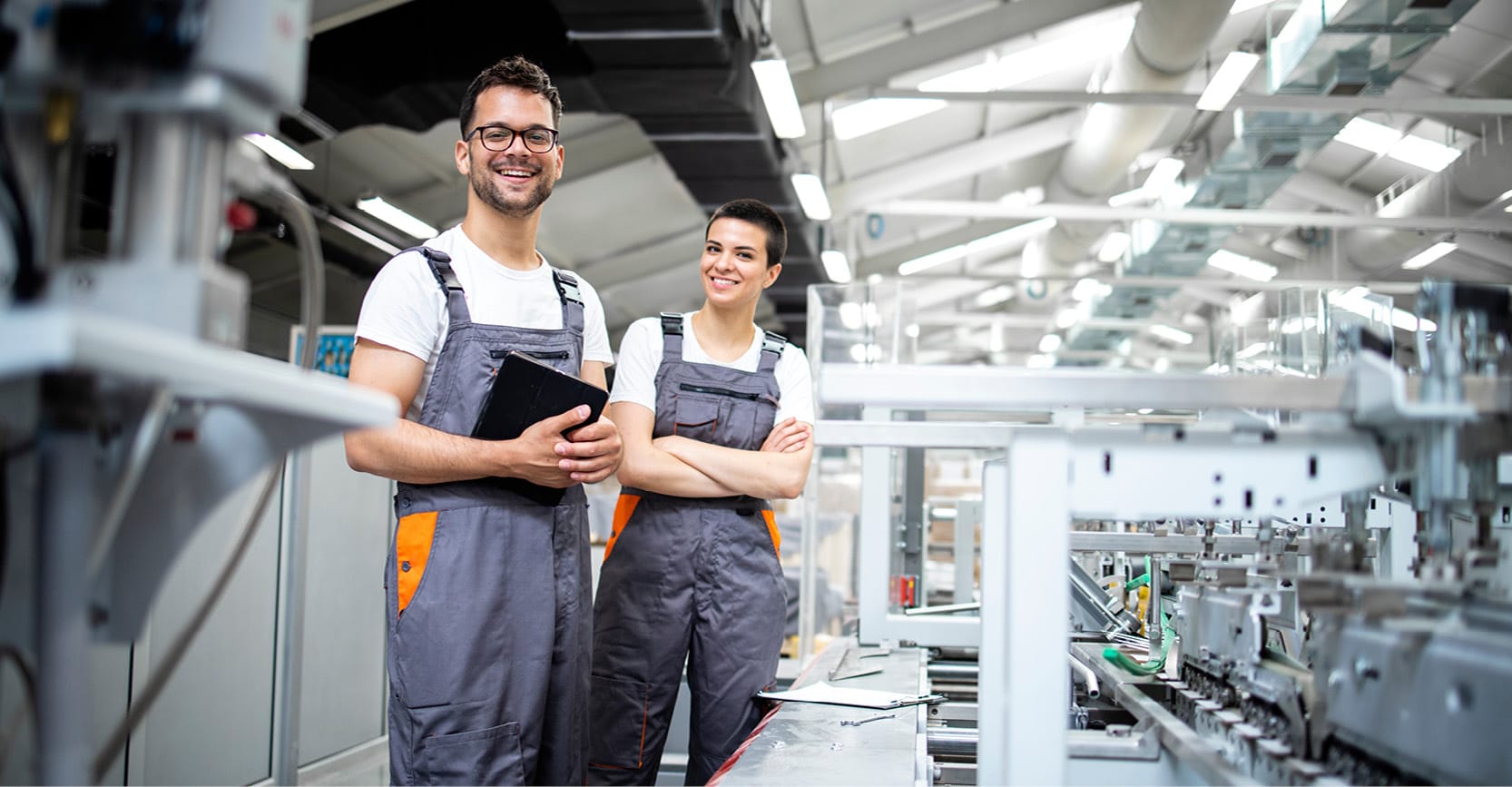 Deux techniciens en salopette souriants dans un atelier de production
