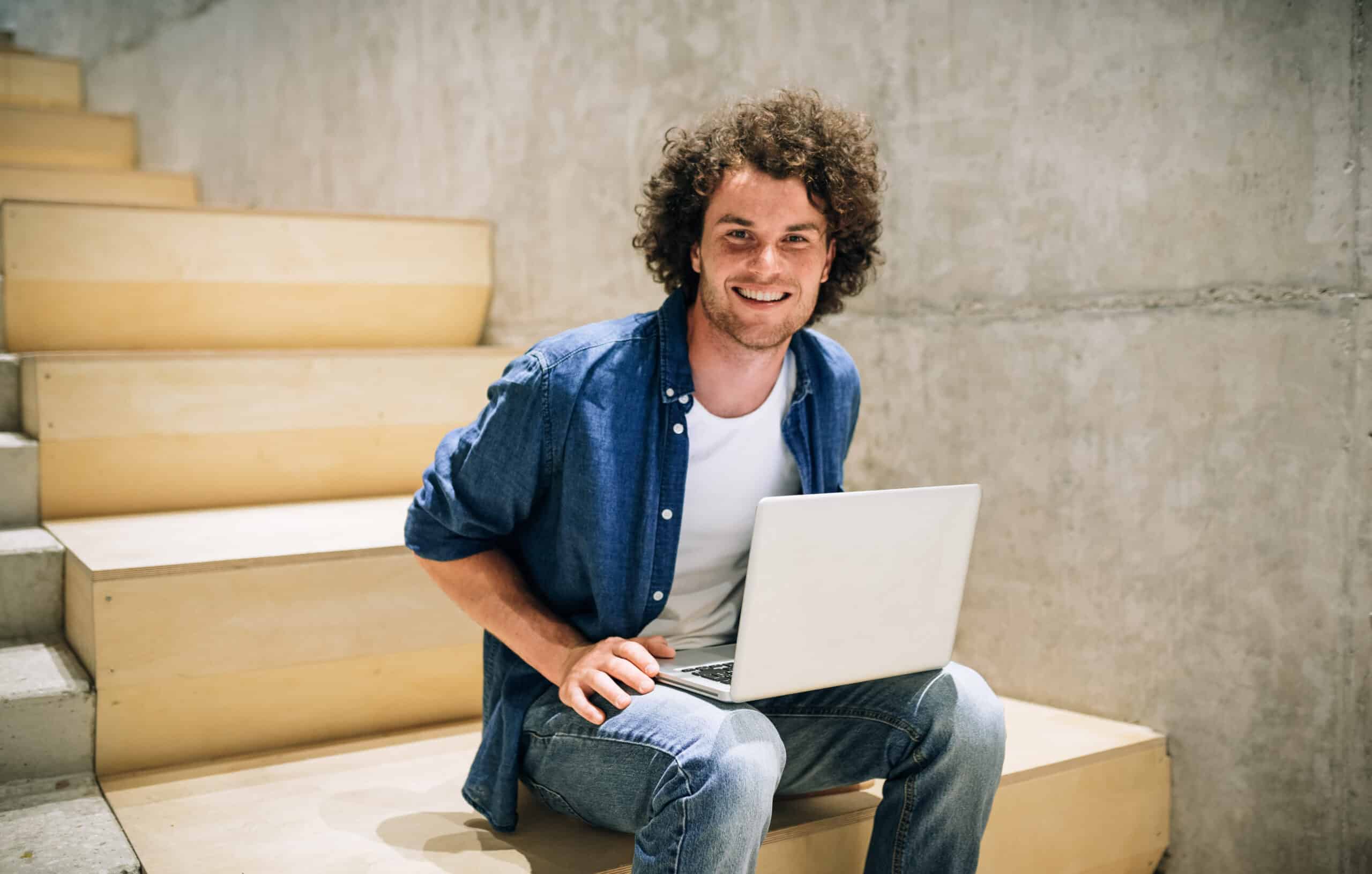 Jeune homme souriant assis sur des marches avec son ordinateur portable