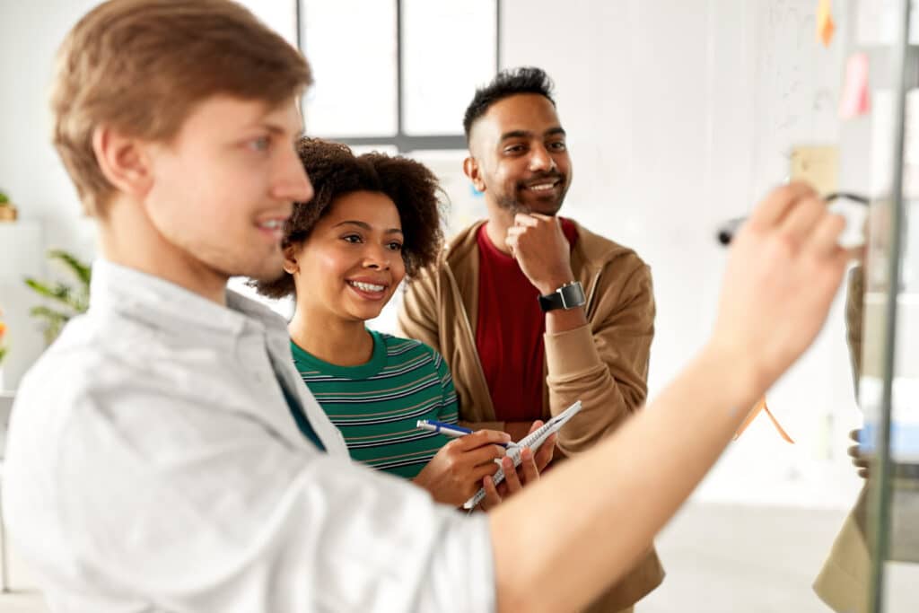 Jeune homme écrit sur un tableau devant deux collègues