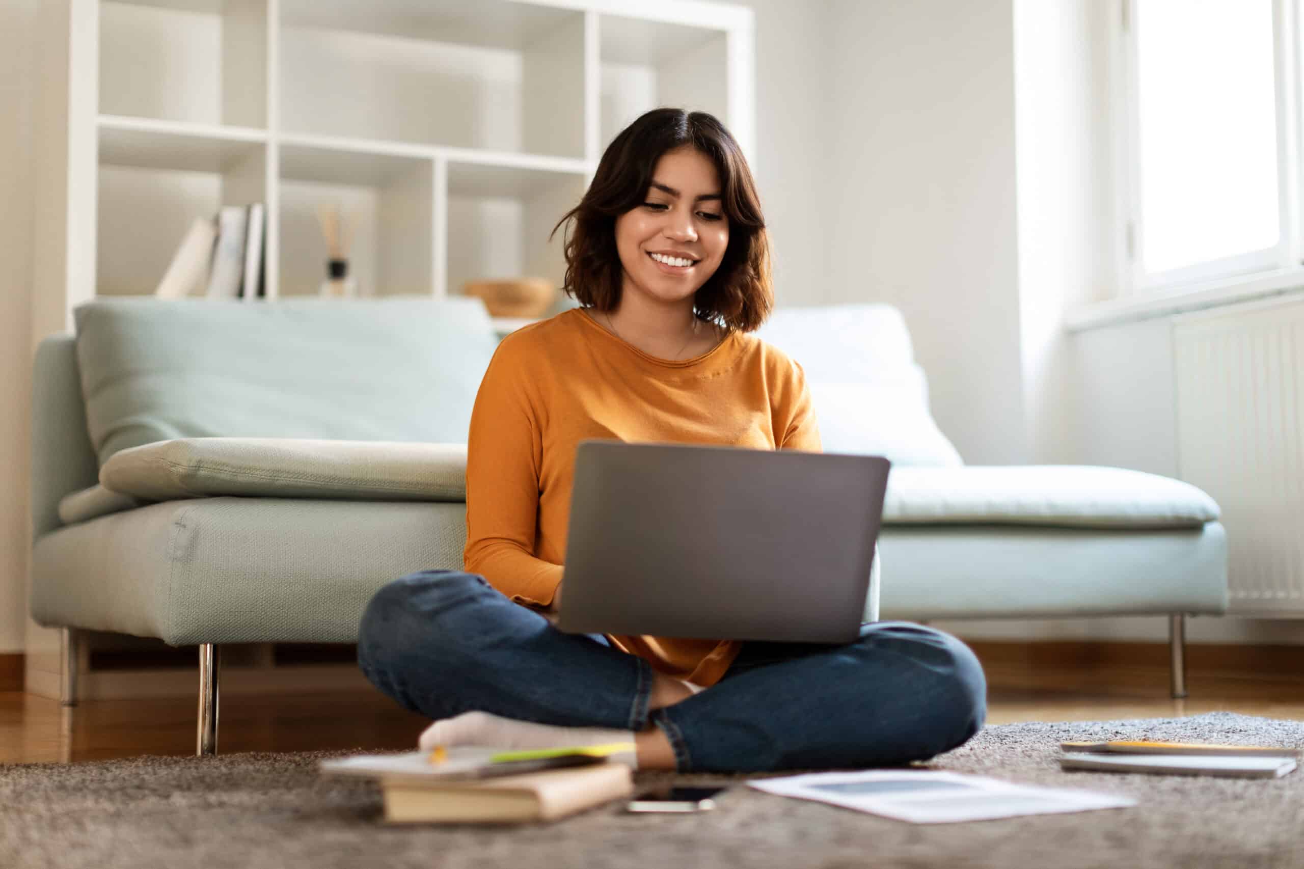 Jeune femme suit un cours à distance sur son ordinateur portable, assise chez elle