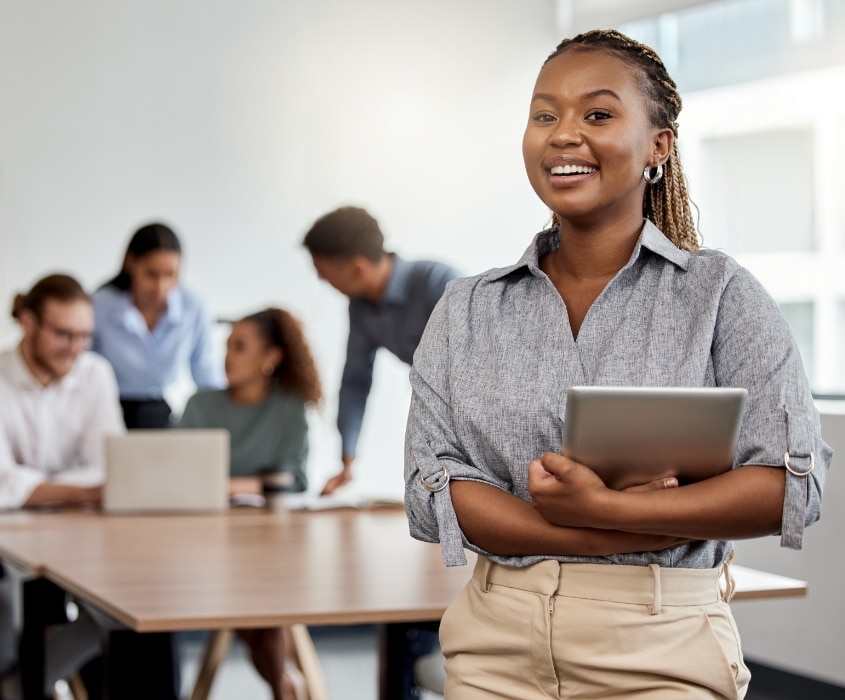 Jeune femme souriante tenant une tablette, collègues en réunion derrière elle