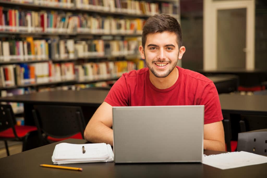 Étudiant souriant devant son ordinateur portable dans une bibliothèque