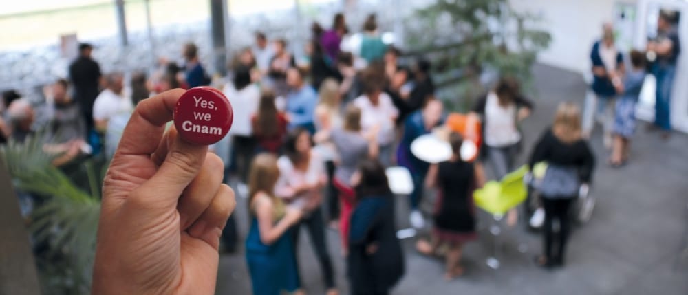 Badge « Yes we Cnam » tenu devant une foule lors d'un événement
