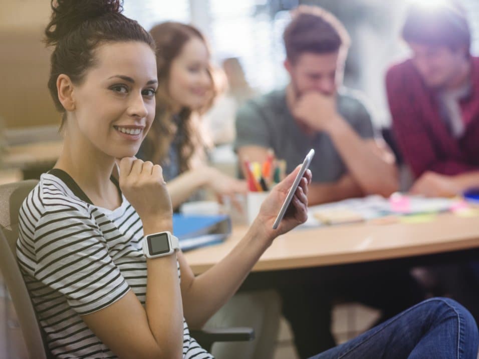 Une professionnelle souriante échange avec des collègues autour d’une table de travail