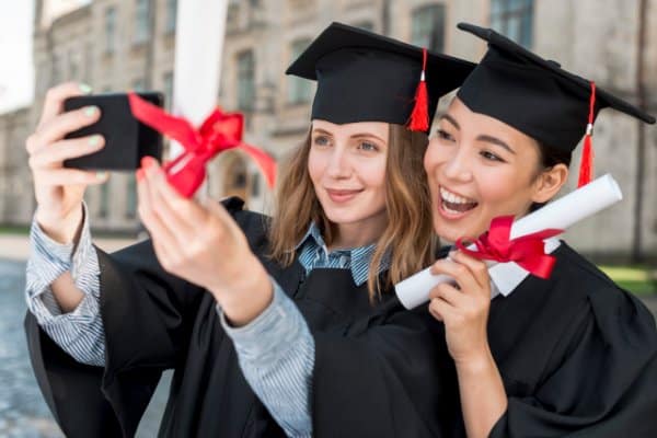 Deux diplômées en toge et toque prennent un selfie avec leur diplôme