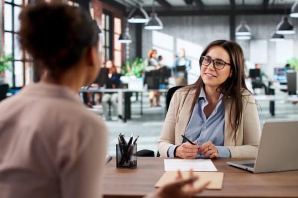 Une femme assise à son bureau écoute une interlocutrice lors d’un entretien