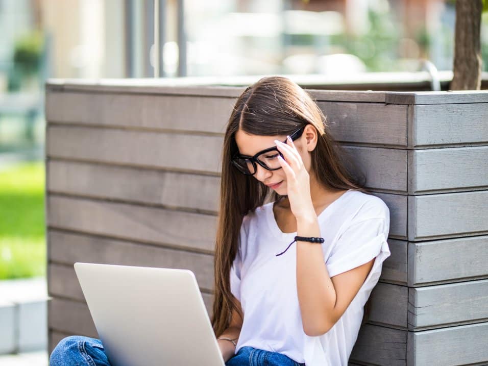 Une étudiante suit un cours sur son ordinateur portable, assise dehors