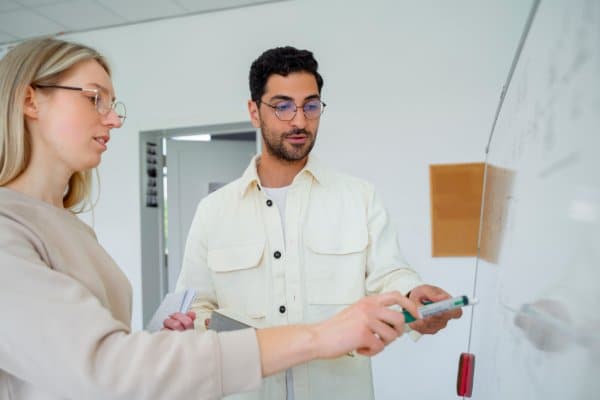 Un formateur explique un document à une participante devant un tableau blanc