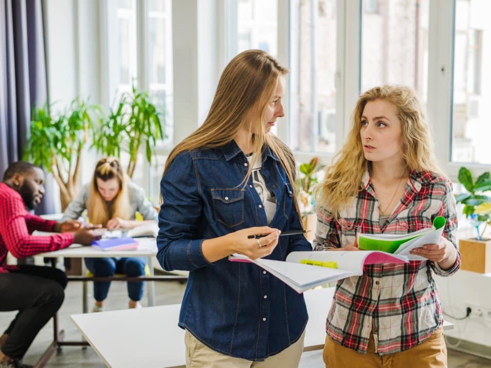 Deux femmes échangent sur leurs études, documents à la main