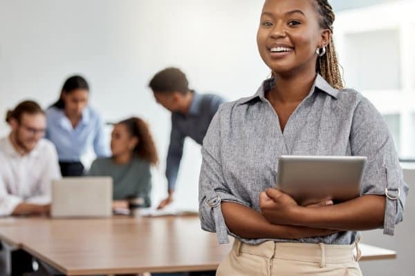 Jeune femme tenant une tablette dans un bureau, devant une équipe au travail