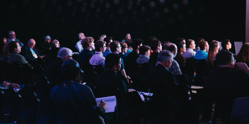 Public assis dans une salle de conférence plongée dans la pénombre