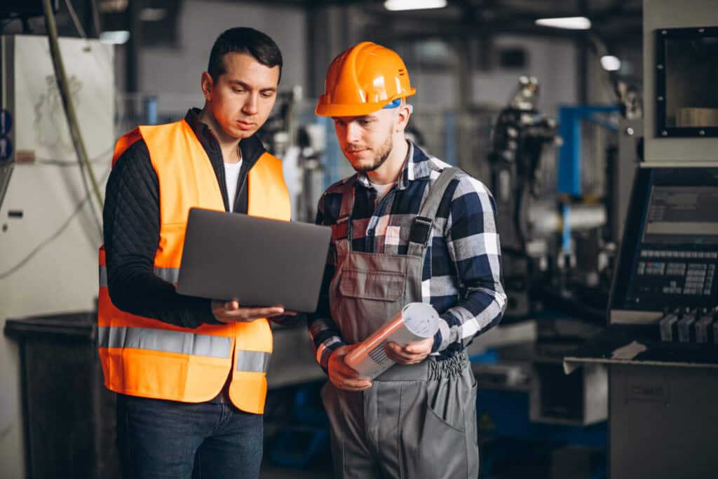 Un tuteur et un alternant échangent devant un ordinateur portable dans un atelier industriel